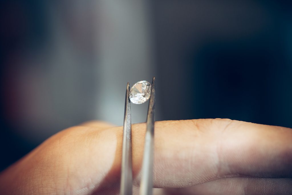 Diamantbestattung. Kleiner Diamant der mit einer Pinzette gegriffen wird. Eine menschliche Hand dient als Stütze.